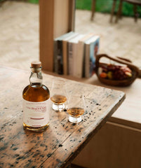 Bottle of Balvenie whisky on a wooden table with two glasses filled with whisky.