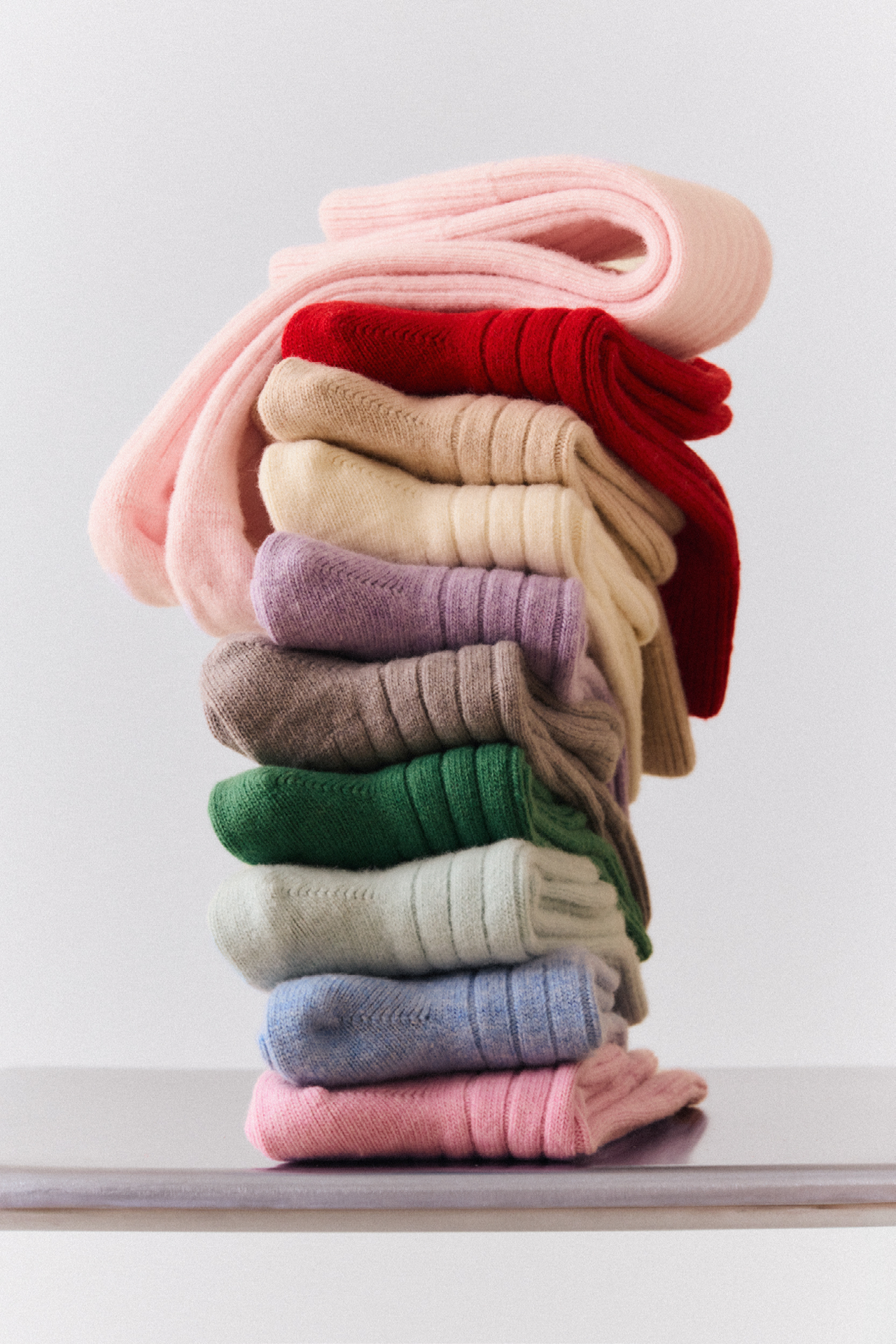 Stack of colourful pink merino bed socks, featuring various shades and luxurious textures.