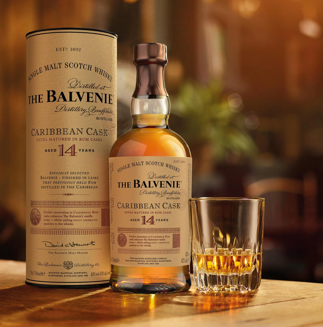 Balvenie whisky bottle and canister with a glass of whiskey on a wooden surface.